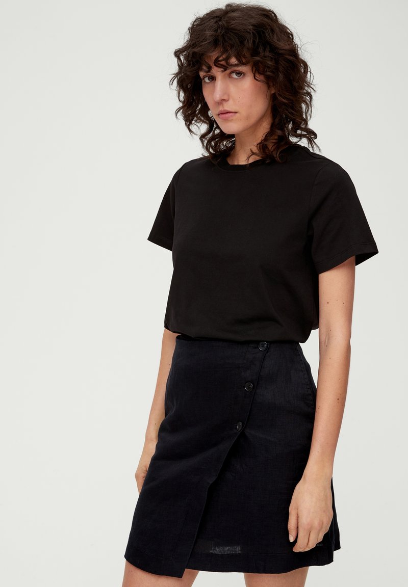 Zwarte T-shirt met korte mouwen gecombineerd met een donkerblauwe linnen wikkelrok met een zijknopenluiting en een subtiele textuur.