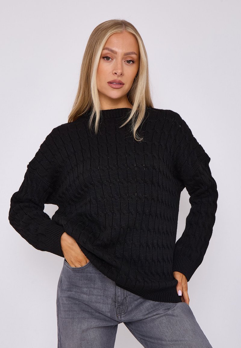 Schwarzer gestrickter Pullover mit strukturiertem Muster, Rundhalsausschnitt und gerippten Bündchen. Kombiniert mit grauen Jeans, die eine lockere Passform haben.