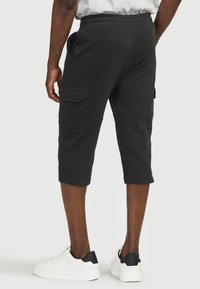 Svarta knälånga sweatshorts med elastisk midja, sidofickor och en patchficka på vänster ben. Slät textur.