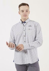 Chemise blanche à boutons avec un motif de pois multicolores, manches longues et un col d'accent bleu foncé. Matériau lavable en machine.