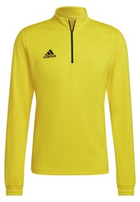Pullover atletico giallo con maniche lunghe, colletto alto, chiusura frontale a mezza zip e logo Adidas nero sul lato sinistro del petto. Tessuto in poliestere liscio.