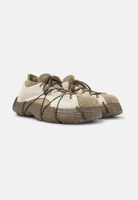 Athletic shoes with a mesh upper in white and tan, featuring a textured brown rubber sole and lace-like accents for tightening.