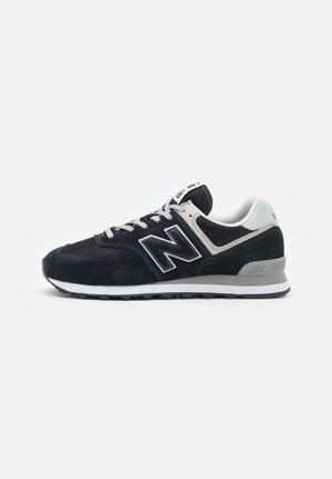 Schwarz-weißer niedrig geschnittener Sportschuh mit Schnürsenkeln, gepolstertem Kragen, strukturierter Sohle und großem „N“-Logo an der Seite.