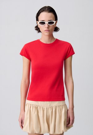 Camiseta de algodón roja con mangas cortas y cuello redondo, combinada con una falda plisada color crema. Diseño limpio, sin patrones o logotipos visibles.