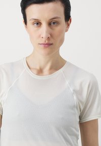 Lett, kortermet treningstrøye i off-white, med teksturert stoff og diskret logo. Glatt, rund halslinje med raglanermer.