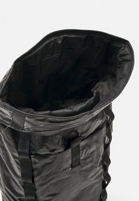 Sac noir, étanche, fabriqué en matériau texturé avec une large ouverture. Présente des sangles latérales et un intérieur doux et doublé. Fini lisse.
