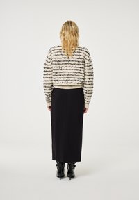 Beige en zwarte gestreepte, textuurtrui met een cropped fit. Gepaard met een lange zwarte rok en glanzende zwarte haklaarzen.