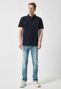 Mörkblå polo skjorta med krage och knapprad, kombinerad med ljusblå denimjeans och vita sneakers. Enkel, avslappnad design.