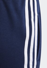 Mörkblå mjukisbyxor med vita sidoränder, mjuk textur, elastiskt midjeband och dold sidoficka för funktionalitet.