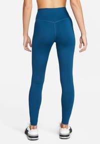 Hoge taille leggings van diep teal stof, met een gladde textuur en een strakke pasvorm, gecombineerd met witte sportschoenen.