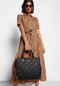 Sac à main matelassé noir avec ferrures et logo dorés, associé à une robe orange longueur genoux ornée d'un imprimé léopard noir.