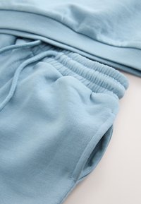 Light blue soft fabric sweatpants with elastic waistband and drawstring, showing side pocket and cuffed hem.