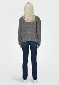 Grå, texturerad tröja med avslappnad passform, tillsammans med mörkblå denimjeans och vita sneakers. Vy bakifrån som visar plaggets detaljer.