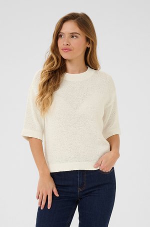 Light cream knit sweater with short sleeves, ribbed neckline, and a relaxed fit, paired with dark jeans. Textured fabric with a loose weave.