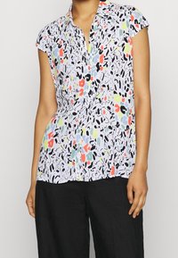 Kurzärmlige Bluse aus leichtem Stoff, mit einem mehrfarbigen abstrakten Muster auf weißem Hintergrund und einer Knopfleiste auf der Vorderseite.