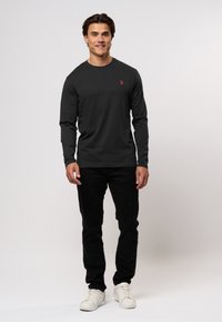 Tricou negru din bumbac cu mânecă lungă, având un mic logo roșu pe piept, asortat cu pantaloni negri și adidași albi. Design simplu, croi lejer.