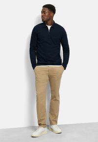 Marineblauwe langesleeve pullover met een half-ritskraag, gecombineerd met licht khaki broeken en witte sneakers, met een eenvoudig ontwerp en een relaxte pasvorm.