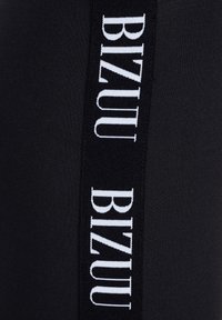 Zwarte leggings met een verticale witte logo "BIZUU" langs de zijkant. De stof heeft een gladde textuur en een aansluitend ontwerp.