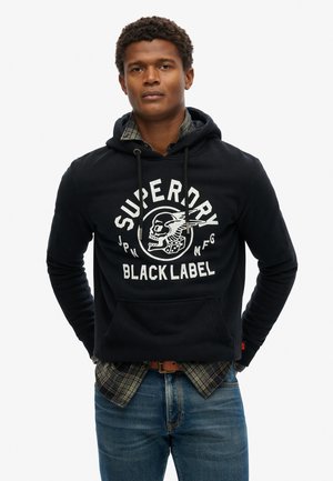 Zwarte hoodie met een frontgraphic van een schedel en de tekst "SUPERDRY BLACK LABEL." Draag over een geruit shirt en combineer met blauwe jeans.