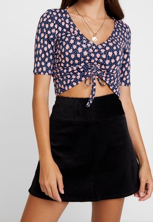 Top court bleu marine avec un motif à pois roses, manches courtes et un détail noué à l'avant ; associé à une mini-jupe en velours côtelé noir.