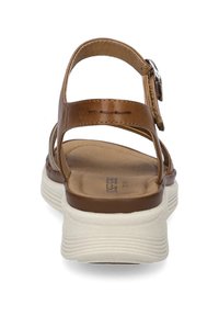 Brown leather sandals with a flat, textured white sole, featuring an ankle strap and buckle detail for secure fastening.