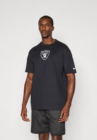 Crni pamučni T-shirt s logotipom Raiders na prsima, upotpunjen okruglim izrezom i kratkim rukavima. Uparen s crnim mrežastim šortsevima.