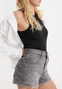 Top negro de canalé combinado con shorts de mezclilla grises de tiro alto, con dobladillo deshilachado y detalles de botones de cobre. Chaqueta blanca colgada del hombro.