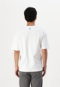 Tricou alb din bumbac, cu mâneci scurte, decolteu rotund și un mic logo negru plasat în partea superioară a spatelui.