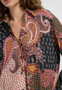 Shirt features a mix of paisley and floral patterns in black, pink, orange, and white, with a collared design and button detail.