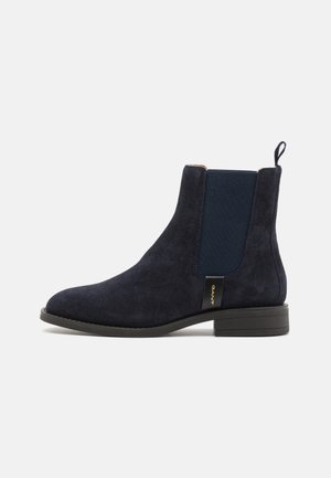 Navy suede Chelsea boot with elastic side panels, low block heel, pull tab on the back, and gold logo detail on the side.