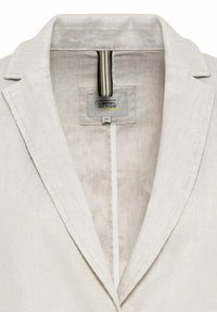 Lichtbeige blazer van een gestructureerde stof, met een notch-kraag en een verticaal gestreepte ophanglus aan de binnenkant. Merkaanduiding zichtbaar.