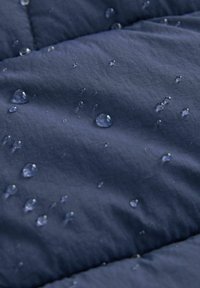 Des gouttes d'eau perlent sur un tissu matelassé bleu foncé, mettant en valeur sa surface et sa texture résistantes à l'eau.