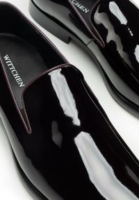 Schwarze Slipper aus Lackleder mit glatter, glänzender Oberfläche und leicht erhöhtem Absatz. Mit eingeprägtem Markenlogo in Weiß.