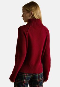 Küpsetatud punane sviiter kõrge soonilise kraega, sooniliste krae, varruka ja äärisega, raglanvarrukatega. Pehme tekstuur ühtlase tausta taustal.