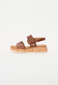 Brown leather sandal with two wide straps, adjustable buckle, cork wedge sole, and textured rubber outsole for grip.