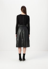 Top negro de manga larga con cremallera trasera, combinado con una falda midi de cuero negra de cintura alta con textura suave y líneas limpias.