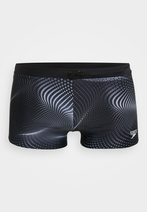 Schwarze Badehose mit einem dynamischen Muster aus weißen Punkten und Wellen, einem Kordelzugbund und einem Logo auf der unteren rechten Seite.