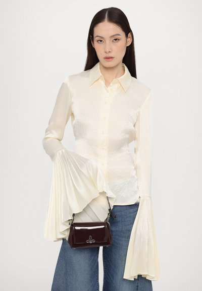 Bluză crem cu mâneci texturate, plisate; închidere cu nasturi. Asortată cu blugi închisi și o poșetă mică, lucioasă, de burgundy.
