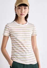 T-shirt rayé en beige et blanc, en coton doux, design ajusté, col rond, avec un petit logo sur la poitrine.