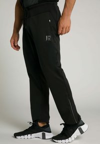 Pantaloni sportivi neri con vita regolabile e coulisse, tasca laterale e logo stampato. Abbinati a sneaker bianche e nere con suole texturizzate.