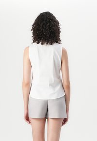 Top bianco senza maniche con una texture liscia, orlo arrotondato, abbinato a pantaloni corti grigi chiari in un design semplice e su misura.