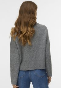 Maglione grigio a maglia con una vestibilità ampia, texture a costine e spalle scese; abbinato a jeans blu a vita alta visibili in fondo.