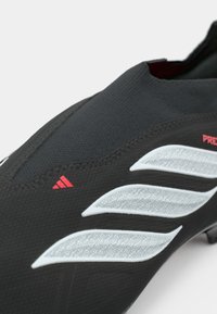 Μαύρο ποδοσφαιρικό παπούτσι με υφασμένο επάνω μέρος, με τρεις λευκές ρίγες και κόκκινη λεπτομέρεια λογότυπου. Κομψός σχεδιασμός με ασφαλή εφαρμογή στον αστράγαλο.