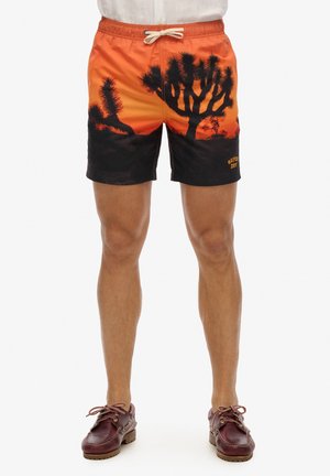 Pantaloni da bagno con un design sfumato arancione e nero e una silhouette desertica. Vita elastica con cordino e dettaglio del logo.
