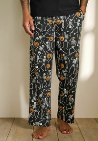 Sorte pyjamasbukser med et Halloween-motiv, der viser hvide skeletter og orange græskar, lavet af blødt, letvægtsstof.
