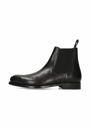 Botín Chelsea de cuero negro con paneles laterales elásticos, puntera redonda y suela plana. Incluye un tirador para facilitar ponerlo y quitarlo.