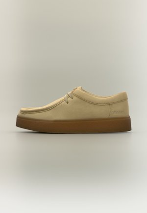 Beige casual schoen met veters aan de voorkant en dikke bruine zool, zijaanzicht op een eenvoudige neutrale achtergrond.