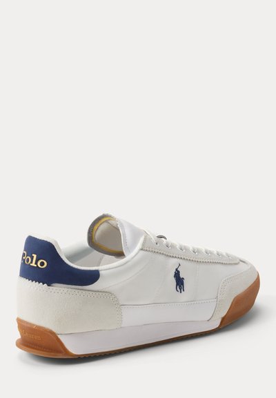 Witte lage sneaker met navy hielstuk, tan rubberen zool en Ralph Lauren Polo-logo geborduurd aan de zijkant.