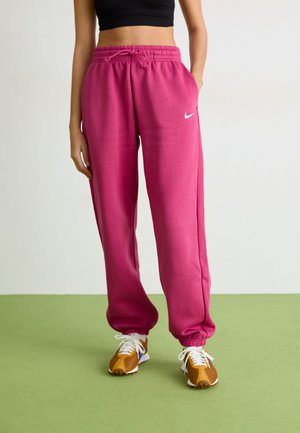 Roze trenirke s elastičnim pojasom i vezicom, s bijelim Nike logom. Uparene s smeškim i bijelim tenisicama.