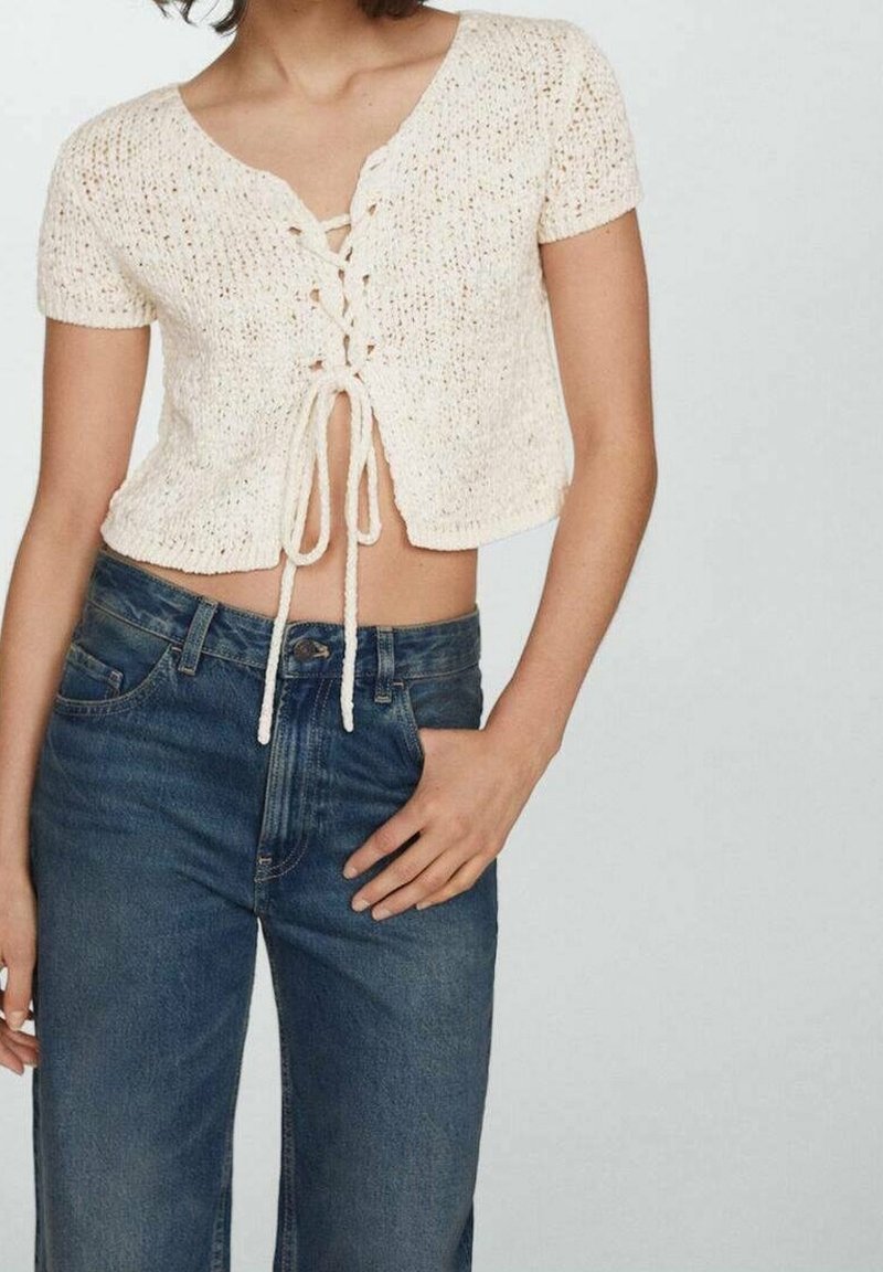 Top court en tricot crème à manches courtes, avec un détail à lacets à l'avant et un motif texturé ; associé à un jean en denim foncé taille haute.